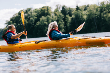 Happy senior active couple kayaking on lake - obrazy, fototapety, plakaty