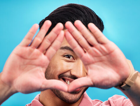 Frame, hands and portrait of Asian man on blue background with smile, confidence and happiness. Perspective, framing and face of happy male in studio for photography, profile picture and vision sign