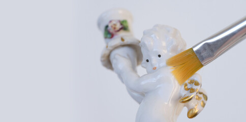 professional restorer at work on white porcelain figurine, candlestick Small cupid of Love with...