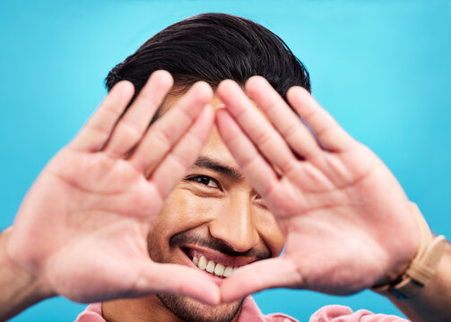 Frame, hands and portrait of happy Asian man on blue background with smile, confidence and happiness. Perspective, shape and face of male person in studio for photography, profile picture and vision