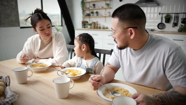 Korean Family Eating And Chatting. Mom, dad and daughter eat corn flakes with milk for breakfast at home.