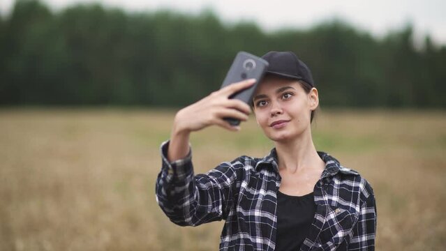 Countryside, pretty woman farmer standing in a field of rye and takes selfie pictures on a smartphone.