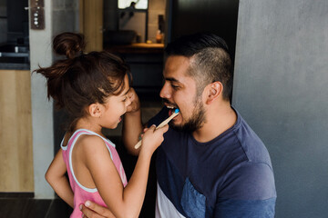 latin young father teaching to his daughter how to brush teeth at home in Mexico Latin America