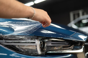 The master in the car service applies a protective armor film to the car body. 