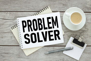 PROBLEM SOLVER, text on an open notebook near a cup of coffee. light wooden background
