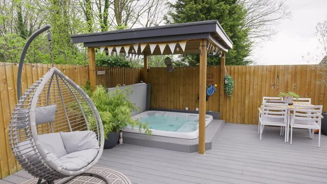 Minimalistic UK summer garden with hot tub, swing chair decking and sun lounger.