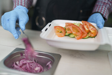 The cook takes Spanish red onion rings with metal tongs. Chef preparing healthy vegetarian lunch box for take away