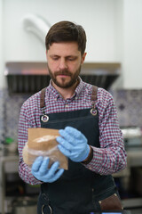 The cook serving pita sandwich for take away in a Greek fast food restaurant. Portrait of male person working in a commercial kitchen