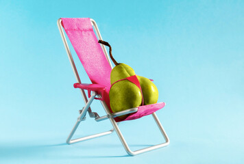 Juicy green pear in pink bikini sitting in sun lounger on blue background. Minimal art poster.