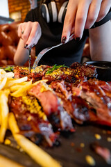 woman hands with fork and knife eating meat ribs in cafe