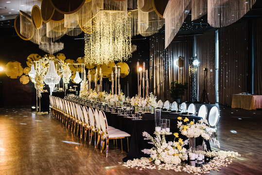 Luxury wedding reception. Table setting, setup. Banquet decoration composition flowers, candles in hall restaurant. Table covered black tablecloth. Trendy decor large chandelier for a birthday party.
