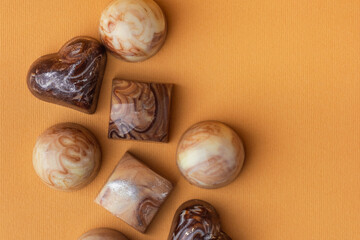 Set of homemade brown chocolate bonbons. Assortment of hand painted candies with marble coating. Mockup with a copy space. Macro shot of  chocolatier products on yellow background. Top view