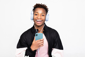 happy cheerful afro american guy wearing modern purple wireless headphones listening to songs standing over white background in studio isolated smiling holding cell phone in hands like microphone.