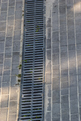 A lattice of a drainage paving system on a footpath made of square stone tiles, close up of a rainwater drainage system