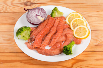 Long raw salmon slices among the vegetables and lemon slices