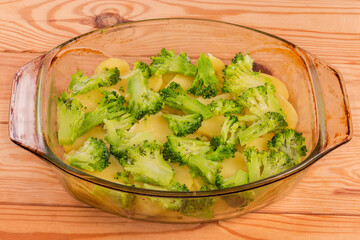 Sliced potato and broccoli in baking dish for casserole preparation