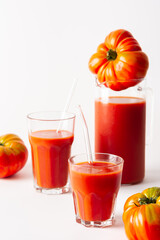 Homemade freshly squeezed tomato juice in glasses and a jug with tomatoes on a white background