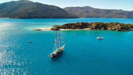 Fototapeta na wymiar Sailing ship near the shoreline of a beautiful tropical island, aerial view