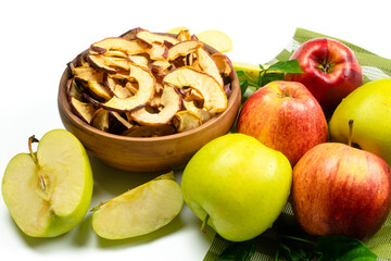 Dry apple slices in a bowl and fresh apples on white background. Dehydrated snacks of apple fruits. Healthy, no sugar sweet food. Candied fruit