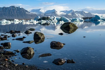 Papier Peint photo Lavable Réflexion Black rocks and boulders reflected in the water of Jökulsárlón glacier lagoon, icebergs and Fellsfjall mountains in the background, Iceland, Vatnajökull National Park, near Route 1 / Ring Road