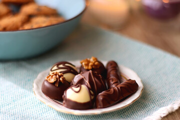 Plate of chocolate pralines, bowl of cookies, cups of tea, glasses of juice and lit candles on the table. Selective focus.