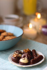 Plate of chocolate pralines, bowl of cookies, cups of tea, glasses of juice and lit candles on the table. Selective focus.