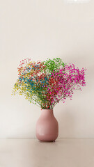 Multicolored flowers in a small pink vase on a white smooth surface