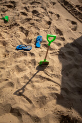 Las chanclas azules de un niño con su pala de jugar con la arena clavada en la playa en un día de...