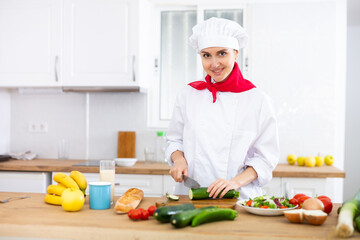 Smiling female chef in white uniform preparing vegetable salad in private kitchen