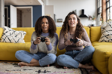Female friends playing video game sitting on floor in loft apartment