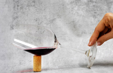 one wine glass supported by one cork, gray background woman hand holding.corkscrew over glass.red tasty beverage.the glass is tilted to one side