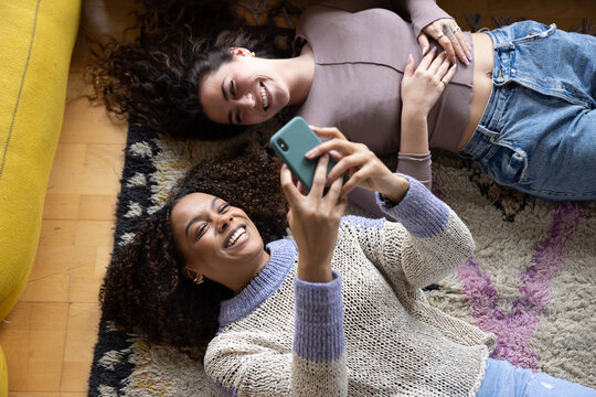 Overhead shot of female friends lying down laughing and looking at smartphone