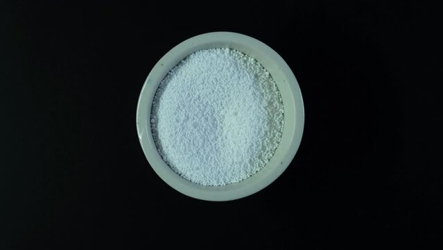 Sodium benzoate, sodium salt of benzoic acid. White crystalline powder in laboratory ceramic dish. Counterclockwise rotation. Food additive E211, Preservative.
