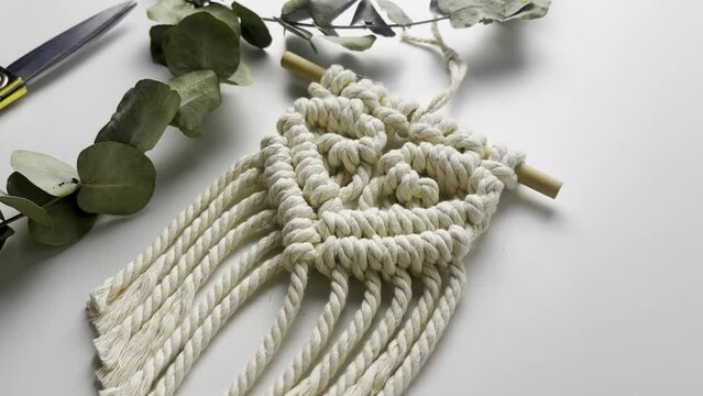 Macram&eacute; wall hanging,  with heart pattern. close up. Slow motion shot. macrame pattern from natural white cotton threads. 