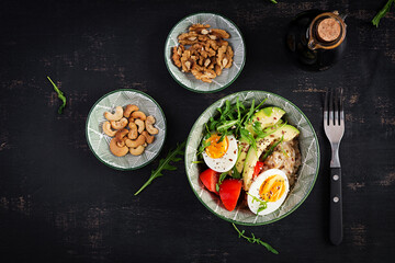 Fototapeta na wymiar Breakfast oatmeal porridge with boiled eggs, avocado, tomatoes and green herbs. Healthy balanced food. Top view, flat lay
