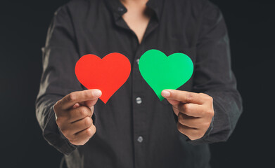 Close-up of hand holding green and red hearts shape symbol while standing on a black background