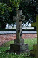 Aged stone cross in a graveyard setting, with a red brick wall in the background