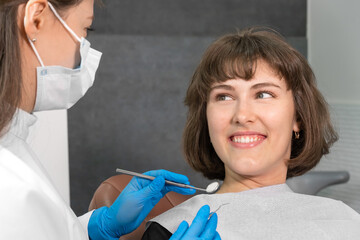 Young smiling woman is sitting in a dental chair and looking at a dentist who is holding dental...