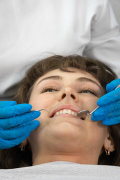 Dental hygienist working with dental instruments checks patient's teeth. Teeth treatment procedure in dental clinic. Examination of teeth with dental instruments. Portrait of woman. Vertical photo
