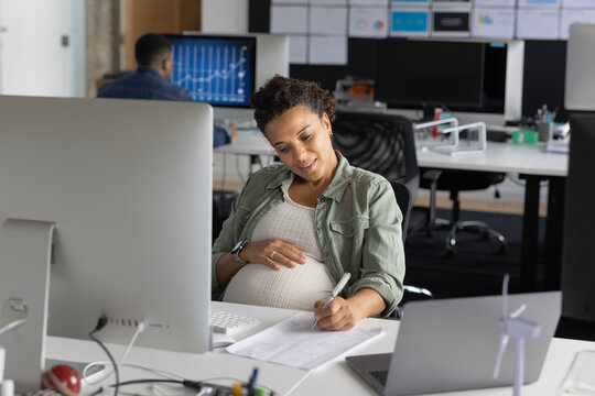 Pregnant businesswoman working at a desktop computer in an office signing paperwork