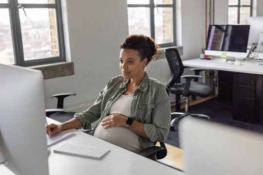 Pregnant businesswoman working at a desktop computer in an office smiling