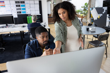 Coworkers meeting round a desktop computer in discussion