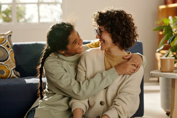 African American happy teenage girl embracing her foster mom while they spending time together at...