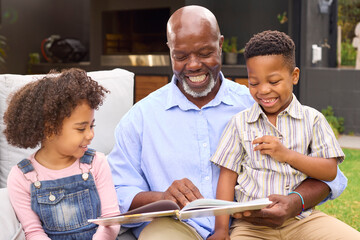 Fototapeta premium Smiling Grandfather Reading Book With Grandchildren In Garden Together