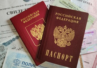 Russian passport and a foreign passport on a stack of personal documents of a citizen. Inscriptions on documents in Russian. Medical insurance policy, driver's license, pension certificate, TIN.