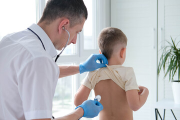 The doctor listens to the breathing of a little boy through a stethoscope. Pediatrician with...