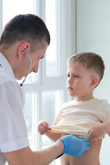 Obraz premium The doctor listens to the breathing of a little boy through a stethoscope. Pediatrician with stethoscope listens to the lungs of a child with bronchitis and cough