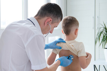 The doctor listens to the breathing of a little boy through a stethoscope. Pediatrician with...