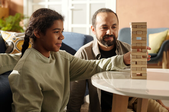 African American teenage girl playing board game with her foster dad at table in the living room