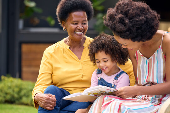 Smiling Multi-Generation Female Family Reading Book In Garden Together